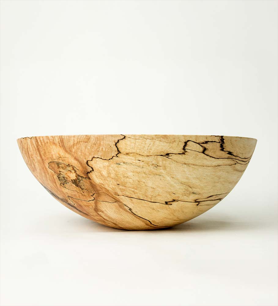 Round spalted maple bowl with distinct dark veining and a gentle curve, photographed against a clean cream background.
