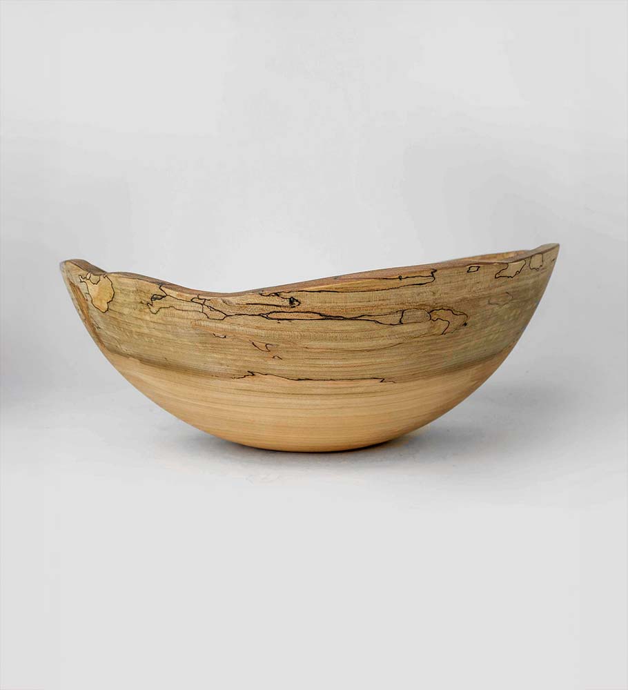 Asymmetrical spalted maple bowl with a natural rim and smooth turned base, resting against a soft gray backdrop.