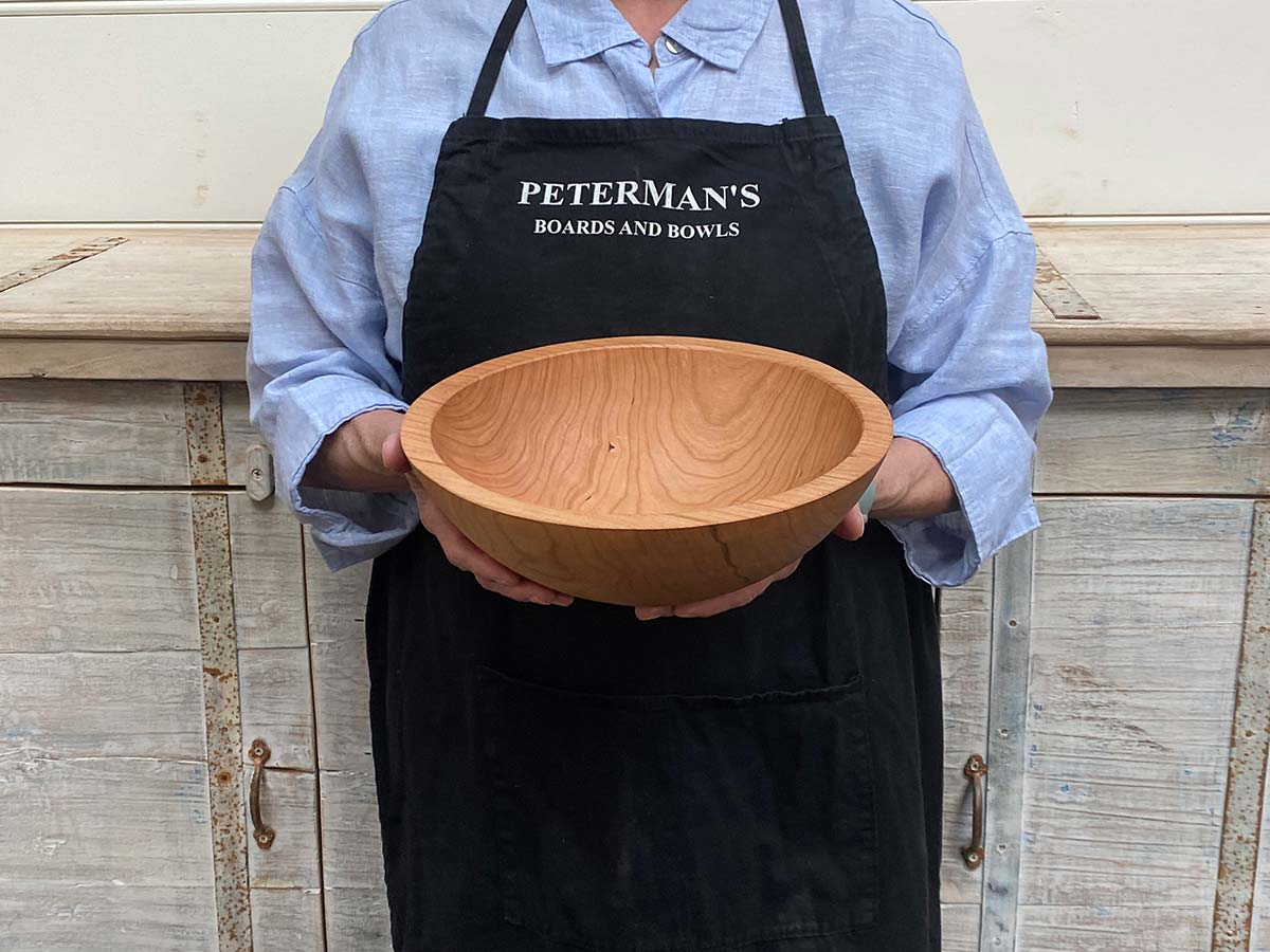 A 10-inch cherry wood round bowl held by a Spencer Peterman craftsperson, the warm tone of the wood glowing in natural light.