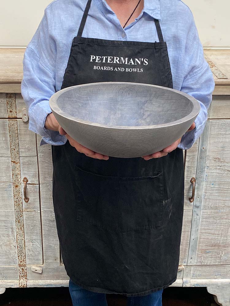 A 13-inch Driftwood Oak round bowl held by a Spencer Peterman employee, featuring the pale, matte finish of aged oak.