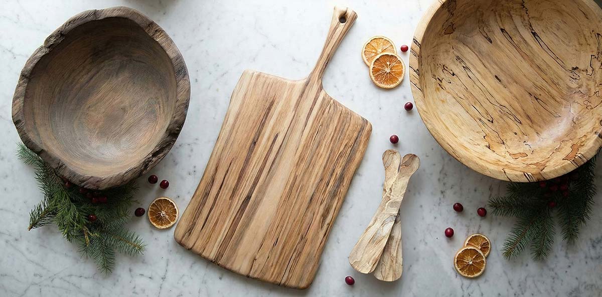 Spalted maple bowls and wooden cutting board arranged on a marble surface with dried citrus and winter greens